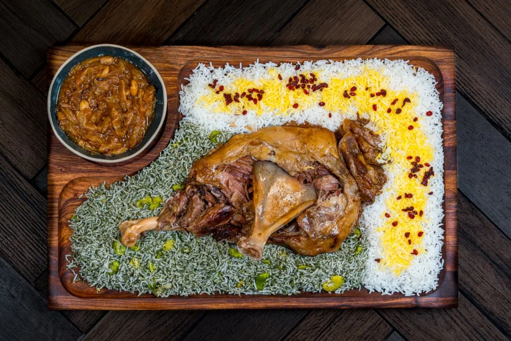 Traditional lamb mandi with saffron rice and curry bowl served on wooden platter