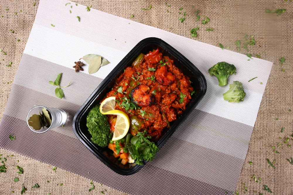 Traditional Persian dish served in a takeaway container with rich tomato sauce, fresh herbs, lemon garnish, and vegetables, showcasing authentic Iranian cuisine in Dubai Creek Harbour.